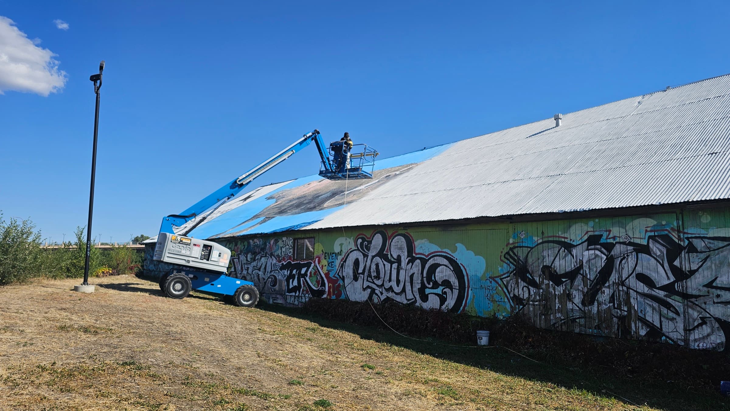 Worker on an elevated platform applying a coating to a large corrugated roof
